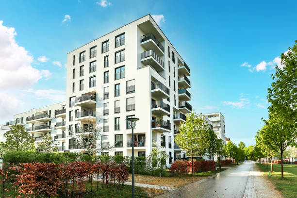 A modern multi-story apartment building with balconies, surrounded by trees and a clear pathway.