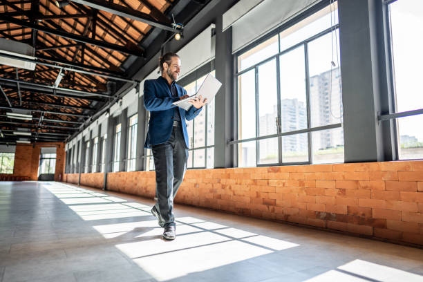 A man walks while looking at his laptop in a bright, spacious office.