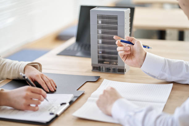 Two people engaged in a meeting, taking notes, and gesturing with pens around model buildings on a desk.