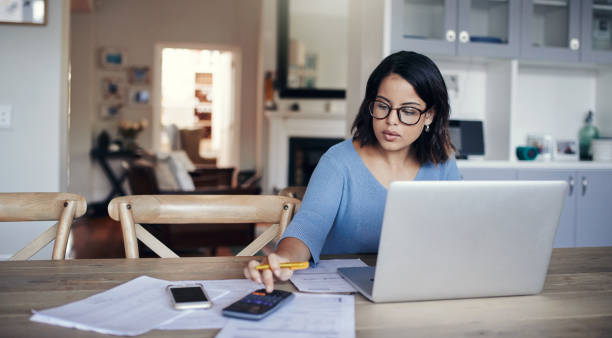 A woman reviewing documents and using a laptop while preparing to buy property in Dubai.