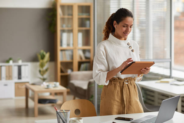 A woman stands in a modern office, engaging with a tablet, likely reviewing Dubai real estate market data.